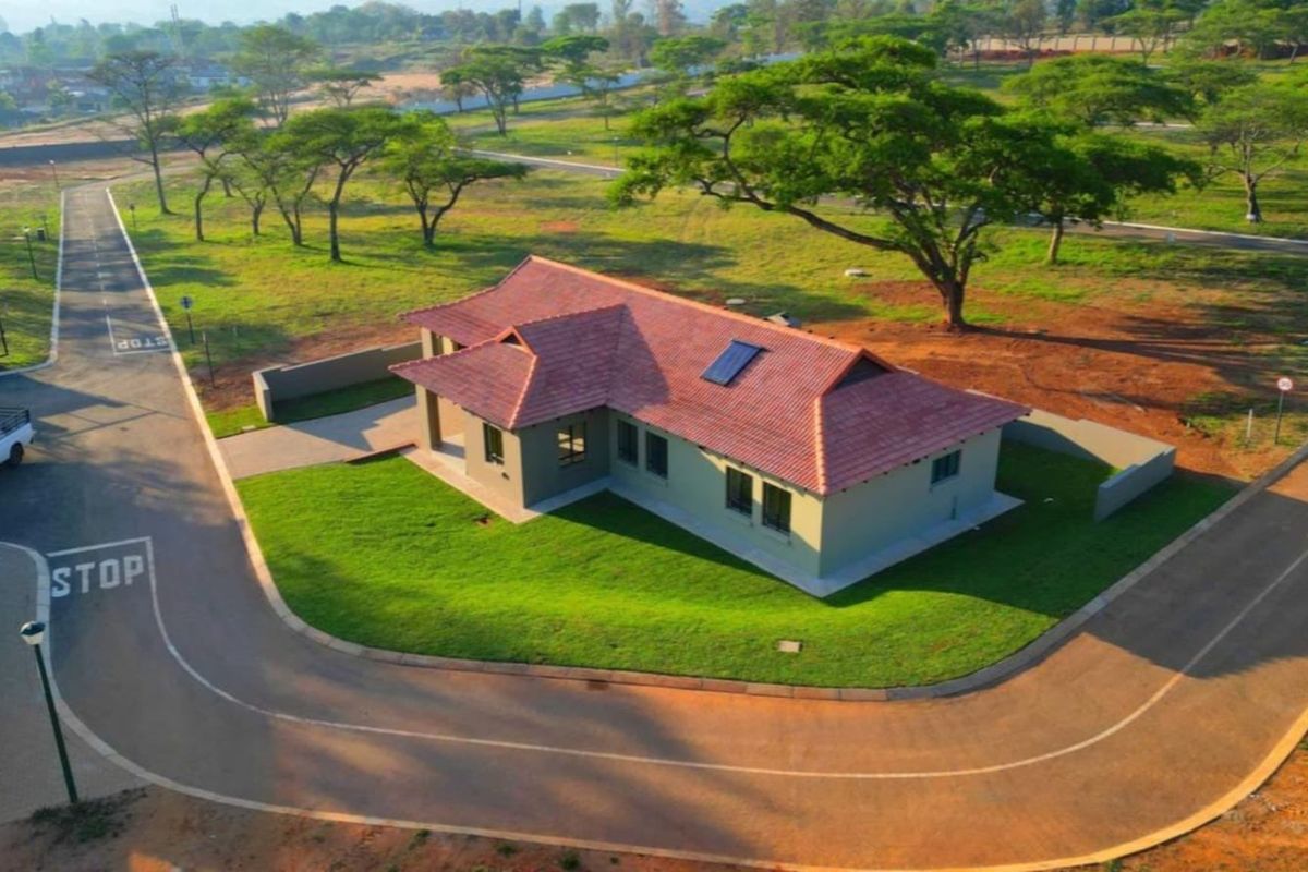 Aerial view of a residential property featuring a tiled roof with solar heating, surrounded by landscaped grounds and paved access roads.