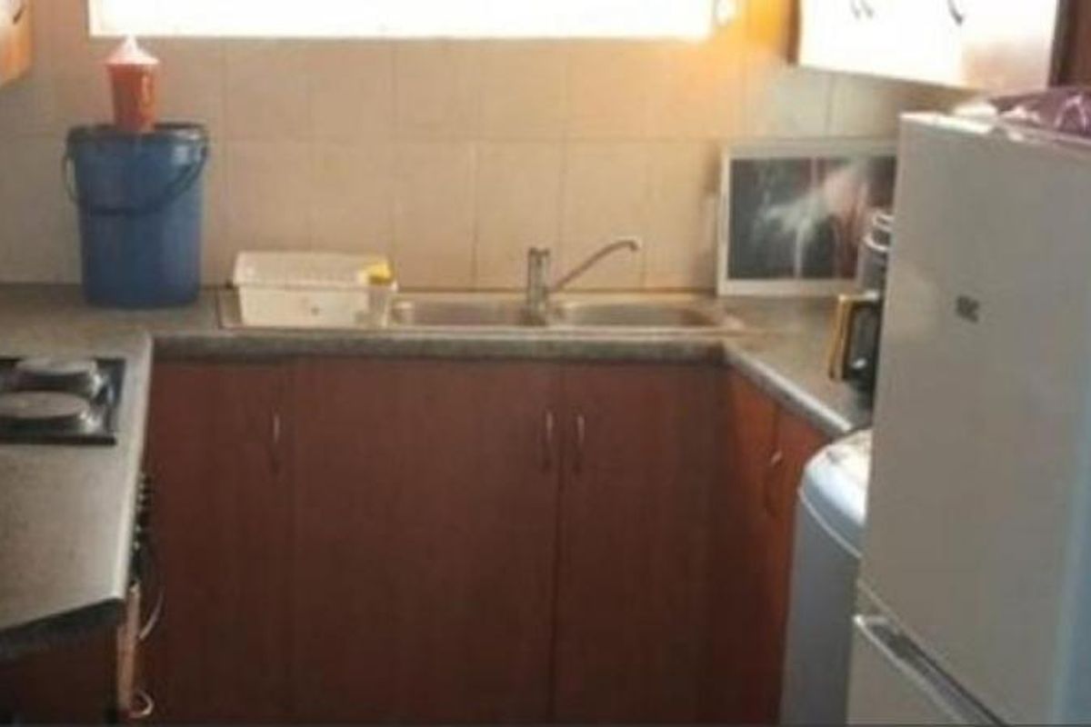 A compact kitchen featuring dark laminate cabinetry, a double bowl sink, and a tiled backsplash, offering a functional layout in need of cosmetic updates.