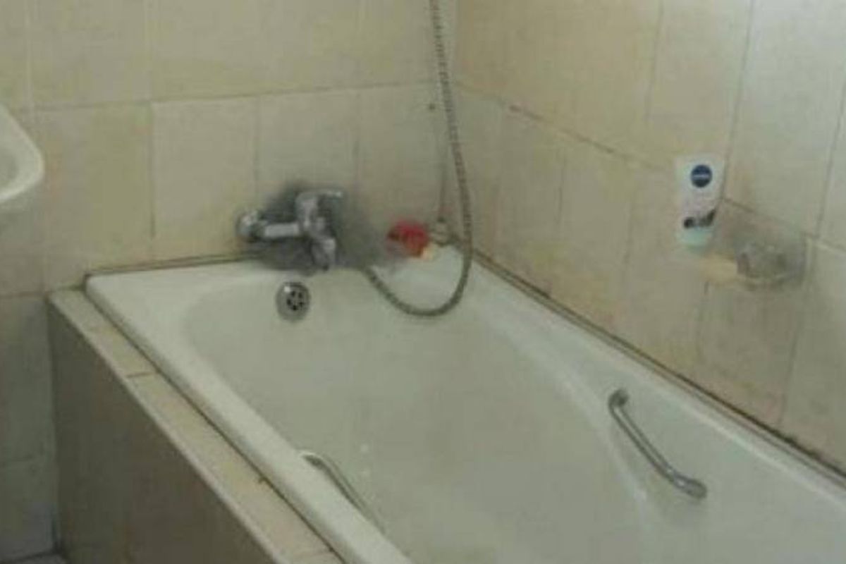 A dated bathroom featuring a standard bathtub with a wall-mounted shower mixer, ceramic wall tiling, and a pedestal basin.