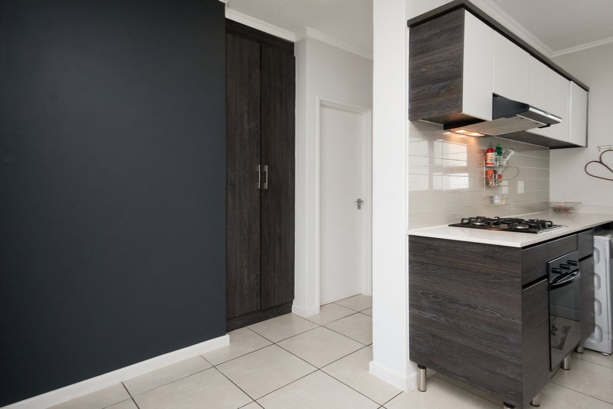 Modern kitchen featuring dark wood-grain cabinetry, a gas hob with extractor fan, built-in oven, and neutral tiled flooring with a contrasting dark feature wall.