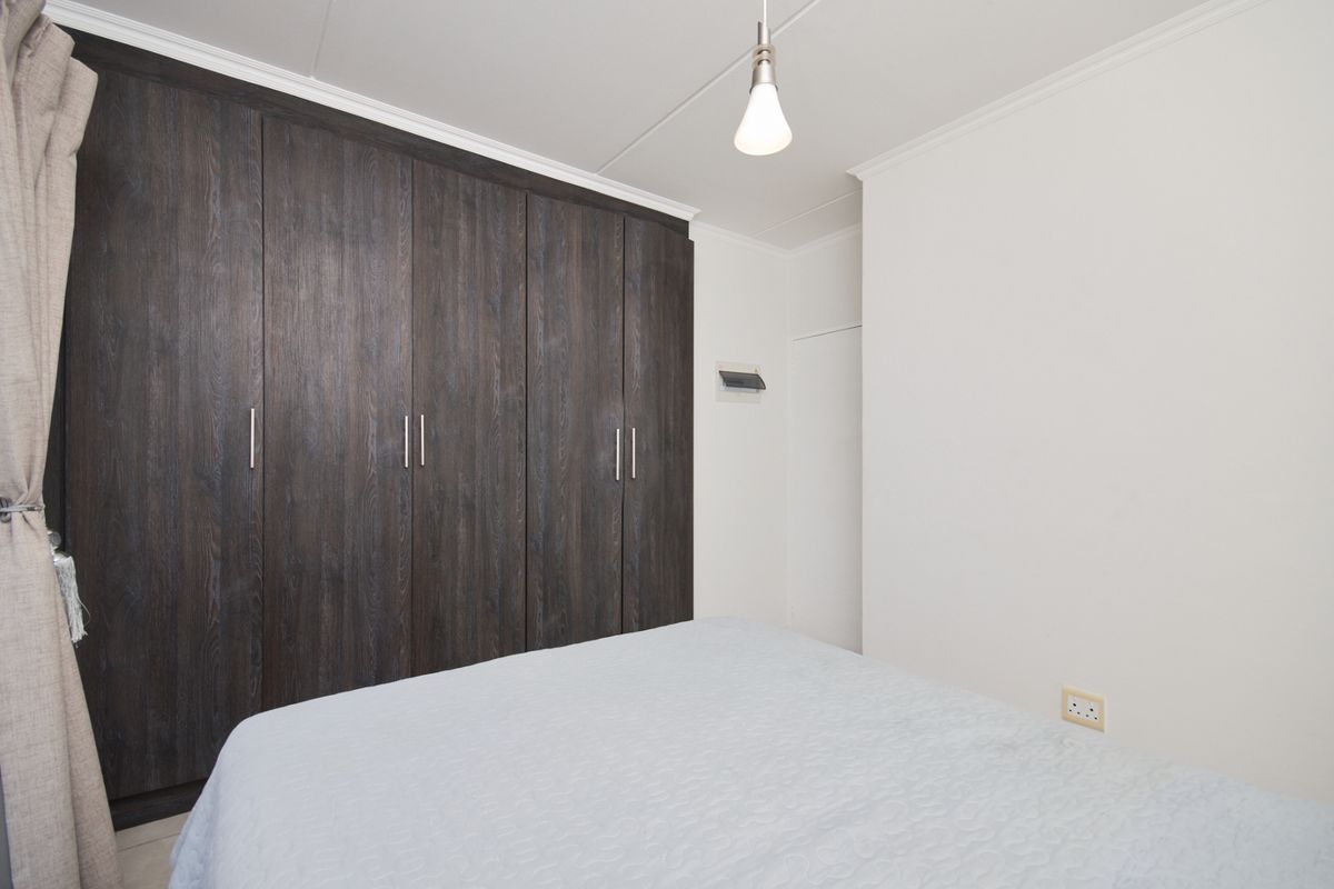 A well-maintained bedroom featuring dark wood-grain built-in cupboards, neutral walls, and classic coving detail.