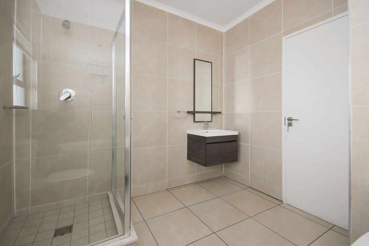 A clean, modern bathroom featuring a glass-enclosed shower, neutral wall and floor tiling, and a contemporary wall-mounted vanity unit.