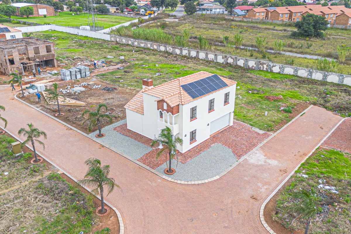 Aerial view of a residential property featuring a tiled roof with solar panels, a brick driveway, and a garage, situated in a developing estate.