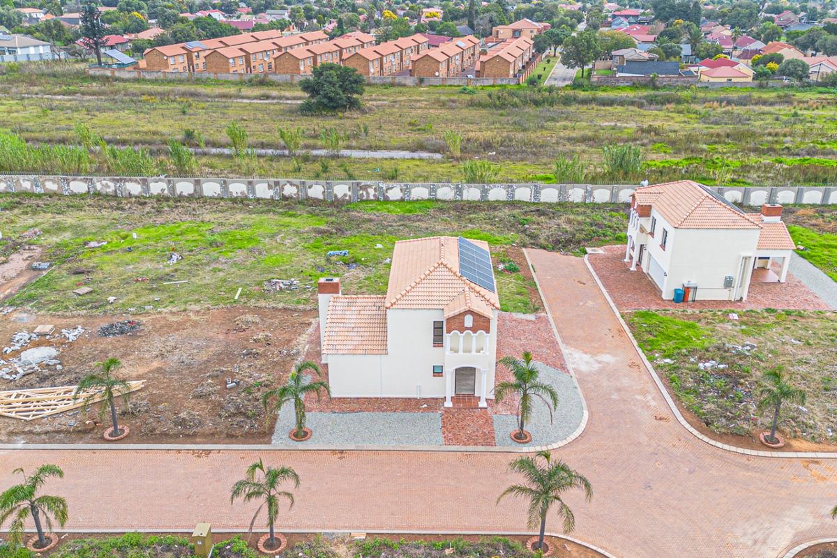 Aerial view of a residential property featuring a tiled roof with solar panels, a paved driveway, and surrounding landscaped grounds in a suburban estate.