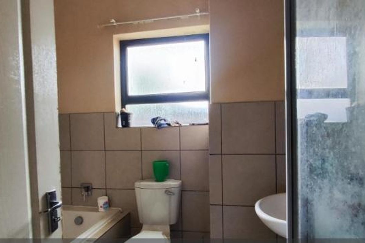 A compact bathroom featuring a shower enclosure, bathtub, pedestal basin, and toilet with neutral wall tiling.