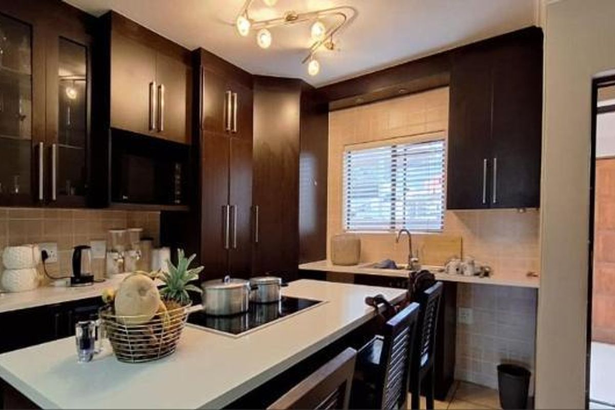 A functional kitchen featuring dark wood cabinetry, stone countertops, a built-in microwave, and an electric hob with a central island.