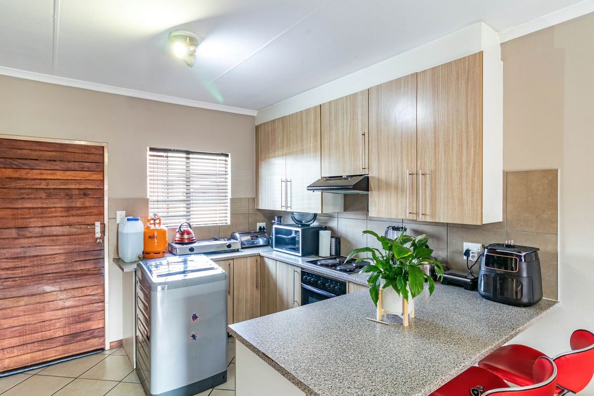 A functional kitchen featuring light wood-finish cabinetry, stone-look countertops, a built-in oven with extractor fan, and tiled flooring.