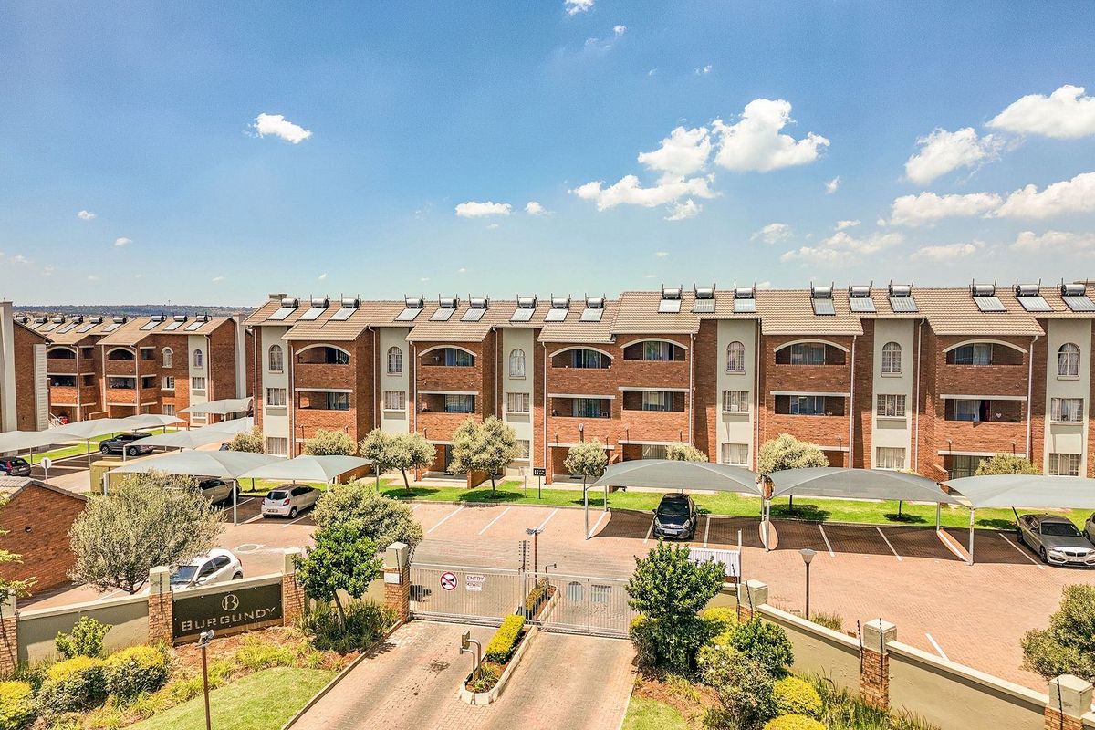 Aerial view of The Burgundy apartment complex, featuring brick architecture, solar water heating systems, secure gated access, and covered parking bays.