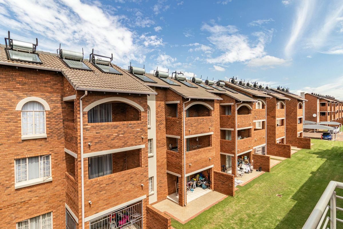 Exterior view of a multi-story apartment complex featuring face brick construction, tiled roofs with solar panels, and private balconies and ground-floor patios.