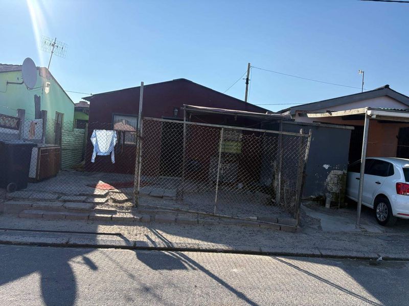 Front exterior view of a residential property featuring a chain-link fence, carport, and paved driveway area.