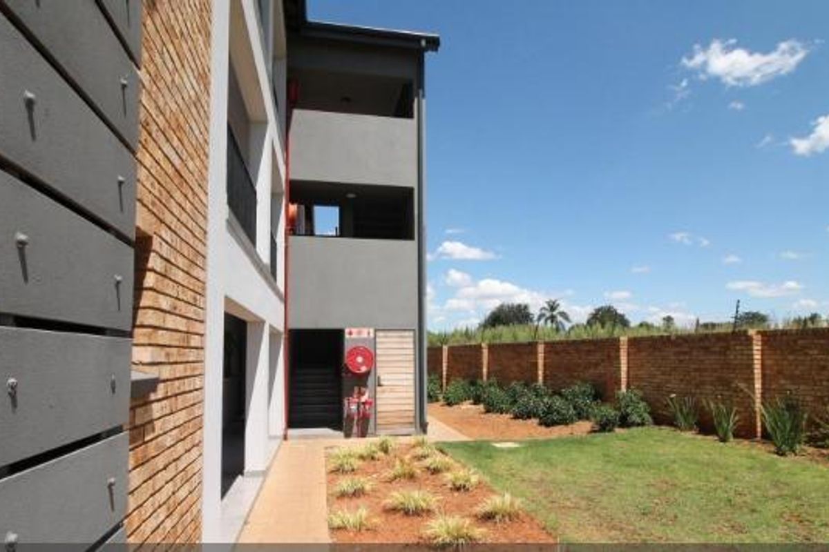 Rear view of the apartment building featuring a paved walkway, landscaped garden, and brick boundary wall.