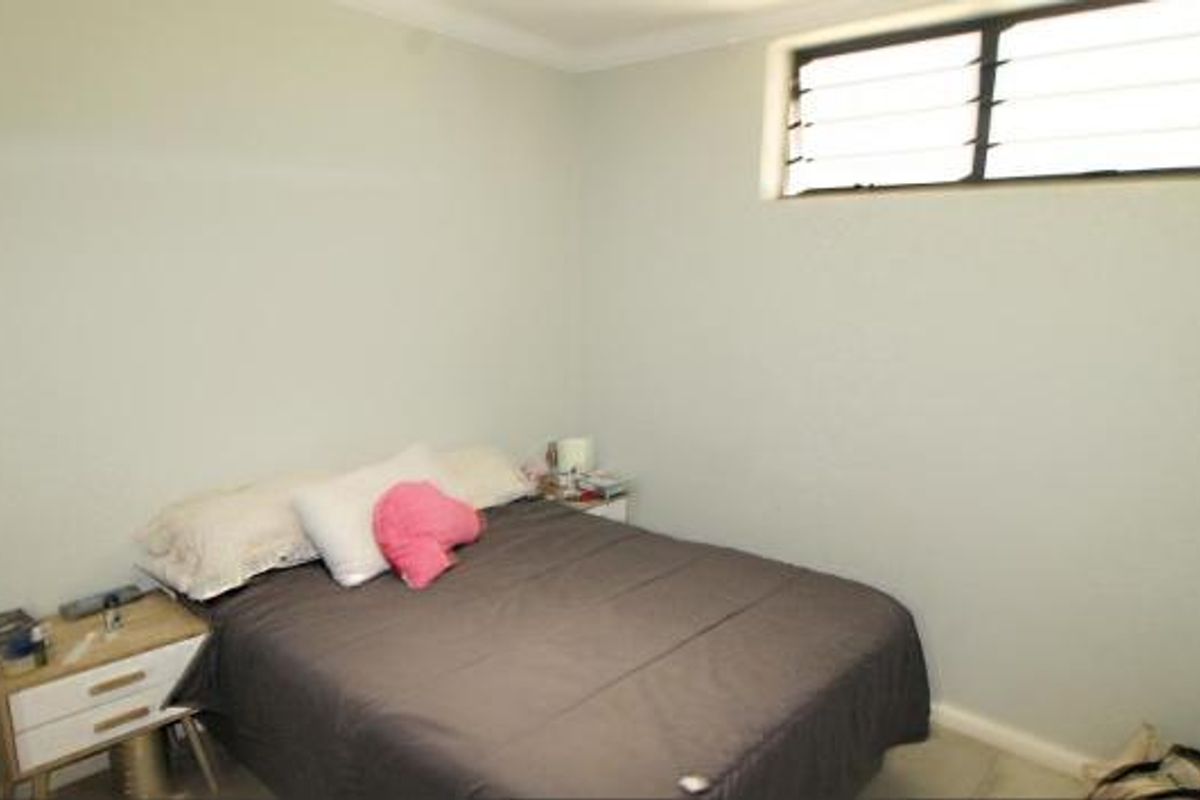 A compact bedroom featuring a high-set louvre window and built-in wardrobe storage.