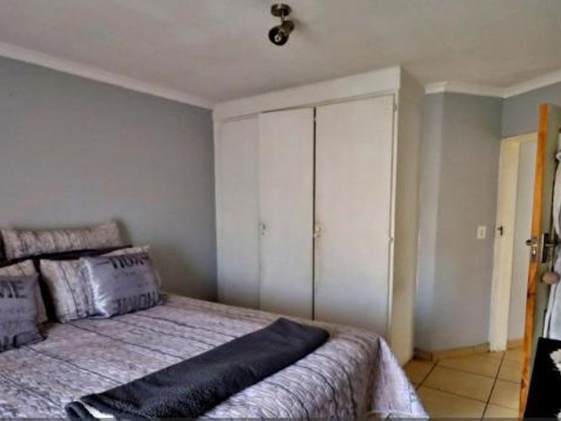 A bedroom featuring built-in cupboards, tiled flooring, and neutral wall paint, providing a functional and well-lit sleeping space.
