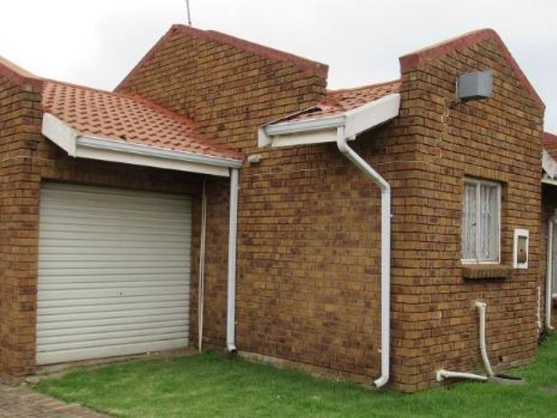 Exterior view of a face brick townhouse featuring a roller garage door, tiled roof, and security bars on the windows.