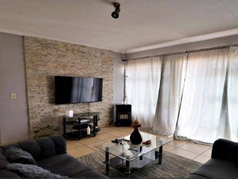 A comfortable living room featuring a textured stone accent wall, tiled flooring, and large sliding doors that provide ample natural light.