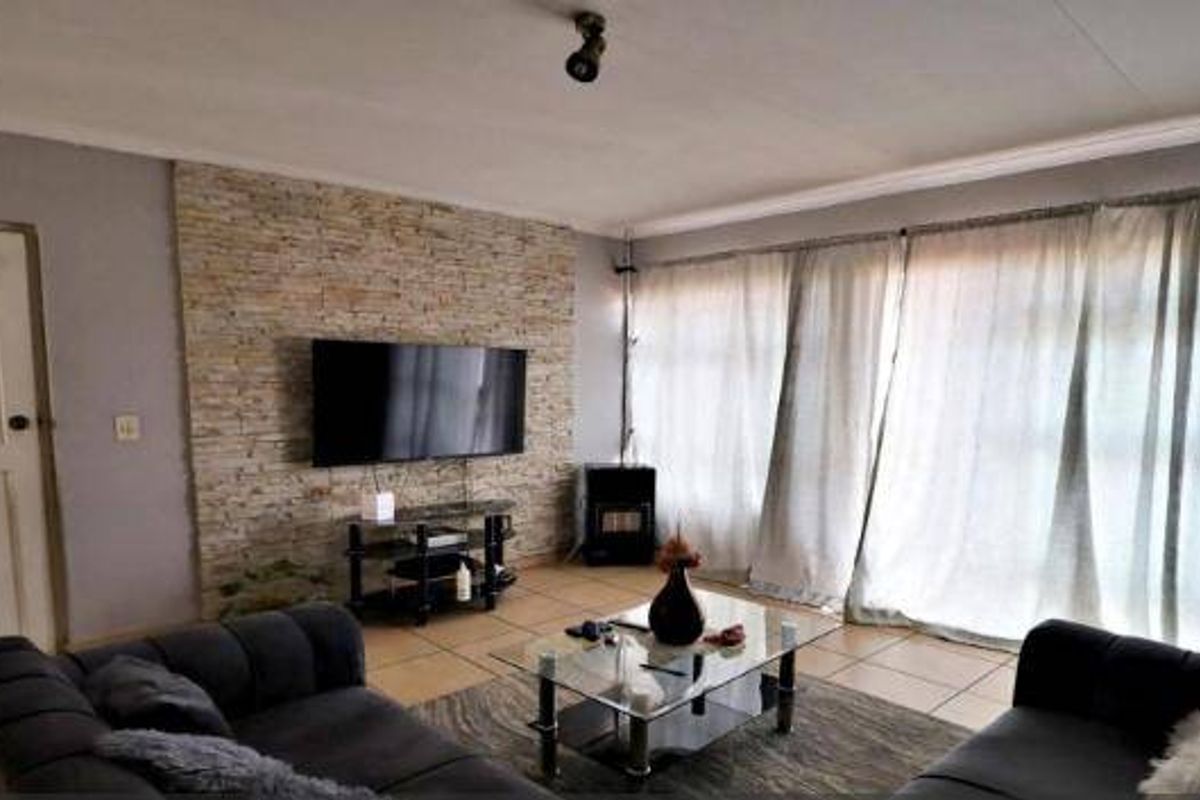 A comfortable living room featuring a textured stone accent wall, tiled flooring, and large sliding doors that provide ample natural light.