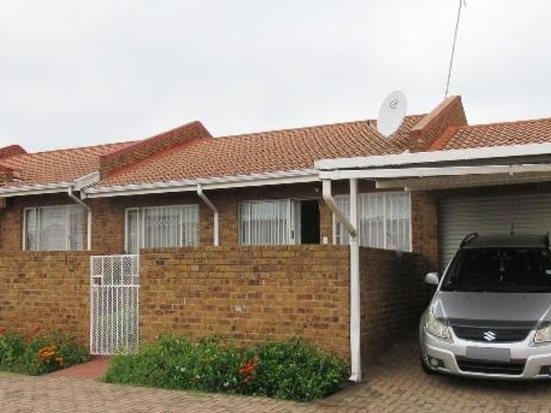 Front elevation of a face brick townhouse featuring a tiled roof, integrated carport, and secure gated entrance.