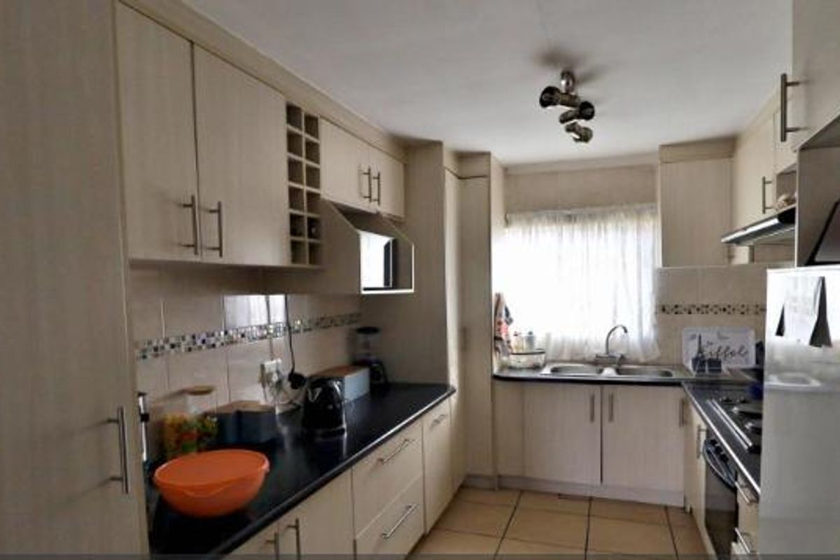 A functional kitchen featuring light-toned laminate cabinetry, a double bowl sink, built-in oven, hob, extractor fan, and tiled flooring.