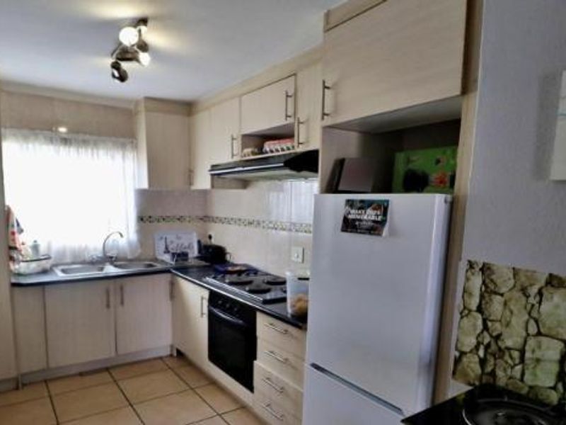 A functional kitchen featuring light-toned laminate cabinetry, built-in oven, electric hob, extractor fan, and a double sink with tiled flooring and backsplash.