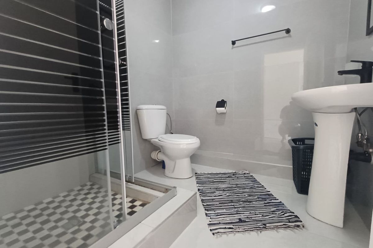 A modern bathroom featuring a pedestal basin, toilet, and a shower enclosure with tiled finishes and contemporary black fixtures.