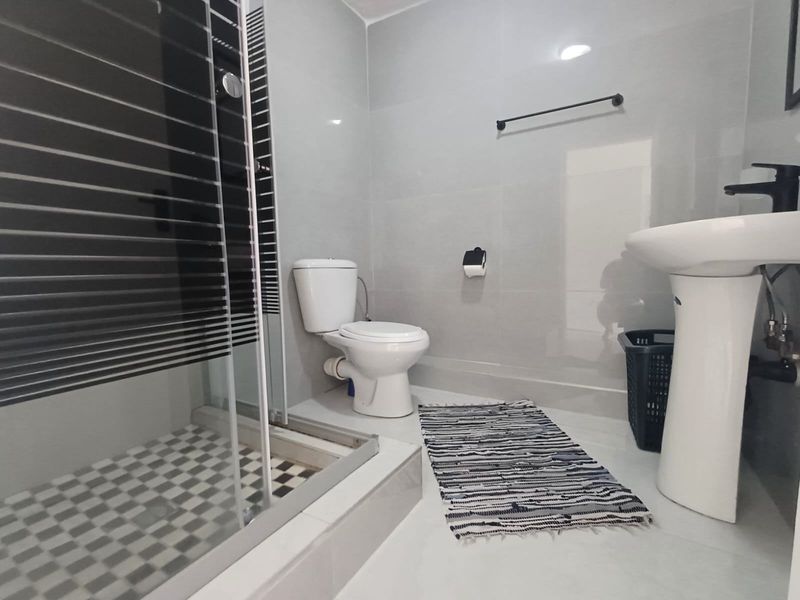 A modern bathroom featuring a pedestal basin, toilet, and a shower enclosure with tiled finishes and contemporary black fixtures.