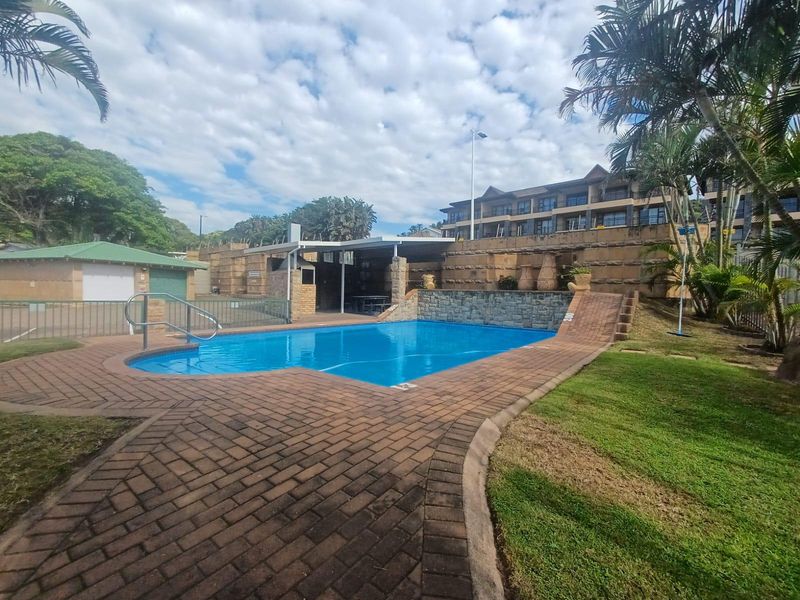 Communal swimming pool area featuring brick paving, a stone retaining wall, and a covered outdoor entertainment space with a built-in braai.
