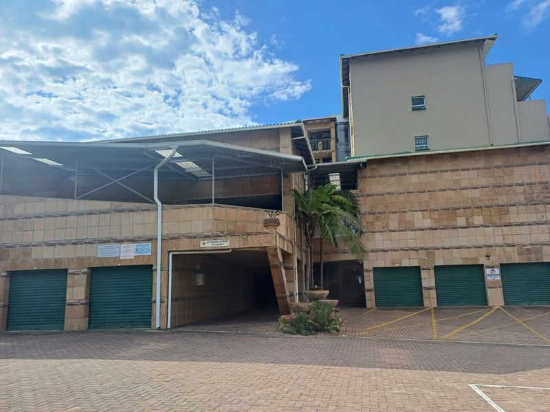 Exterior view of an apartment complex featuring multiple garage units with roller shutter doors and a paved driveway area.