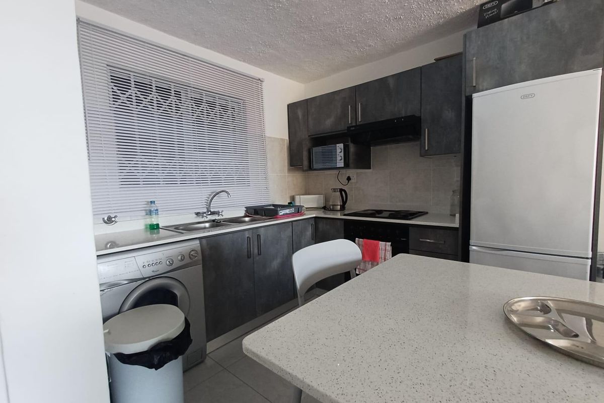 Compact kitchen featuring dark grey cabinetry, stone countertops, integrated hob, extractor fan, and a stainless steel sink with a window security gate.