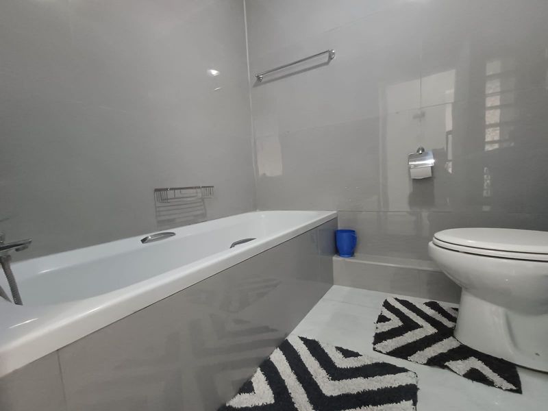 A modern bathroom featuring grey wall tiles, a built-in bathtub, and a standard toilet.