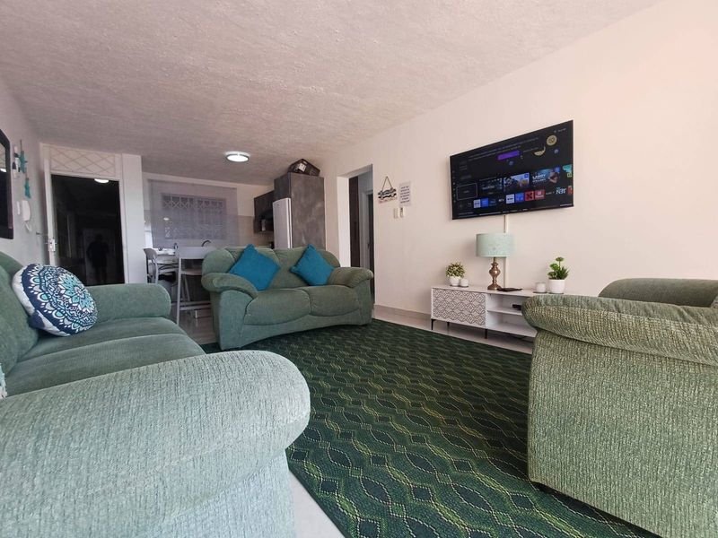 Open-plan living area featuring a lounge space flowing into a kitchen, with recessed lighting and wall-mounted television connectivity.