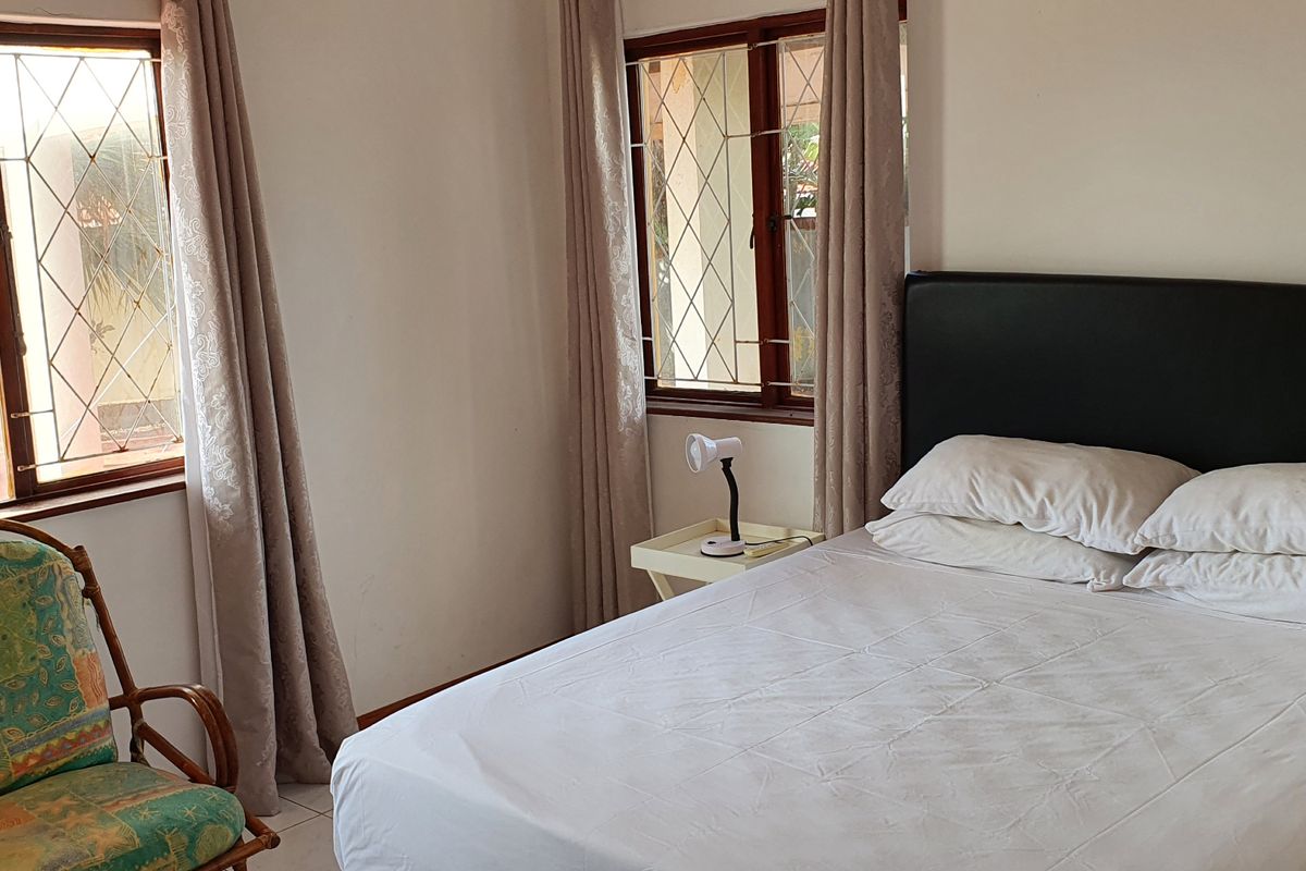 A bedroom featuring tiled flooring and windows fitted with security bars, providing natural light and a functional layout.