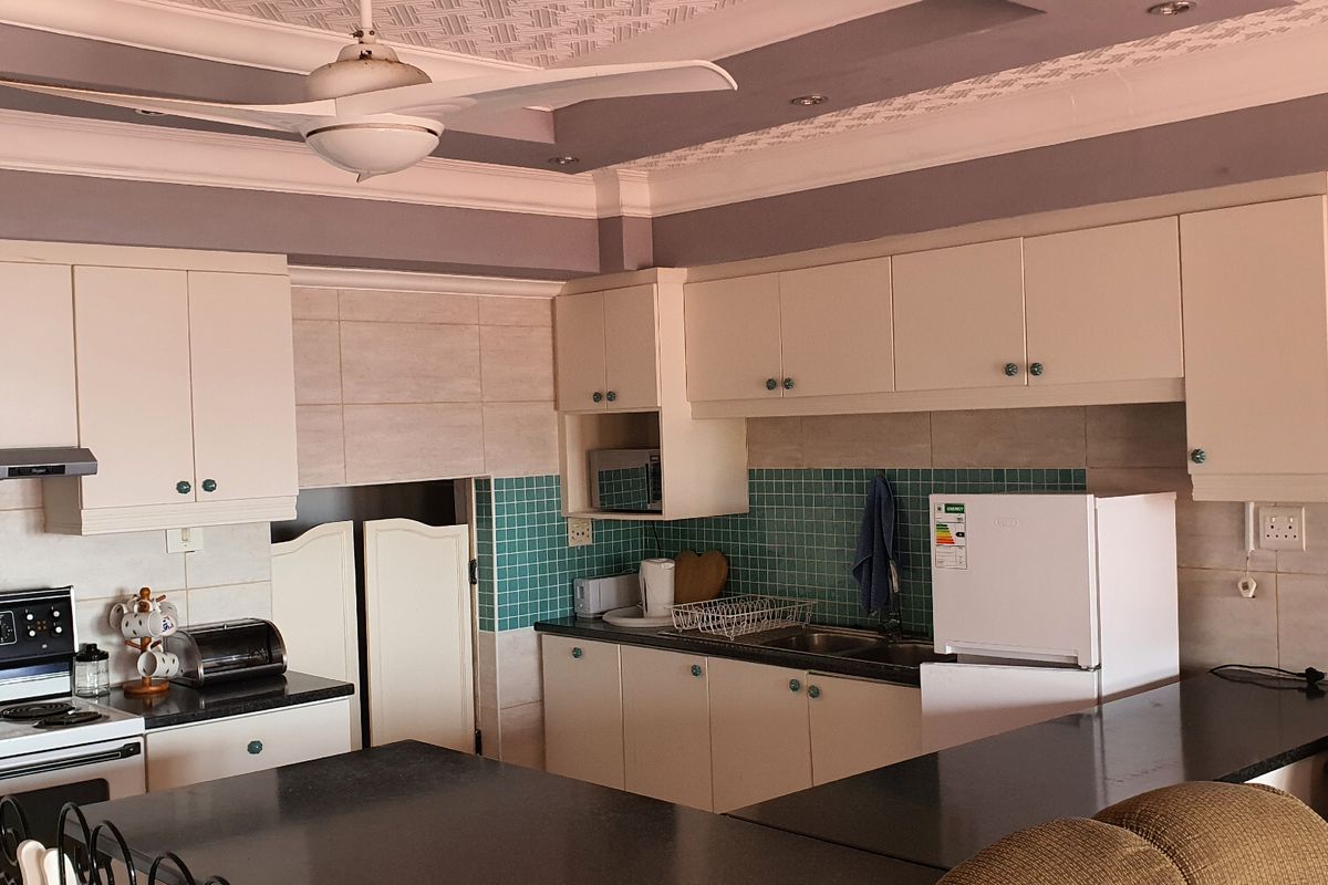 A functional kitchen featuring white cabinetry, granite countertops, a tiled backsplash, and a ceiling fan, offering a practical layout for daily use.