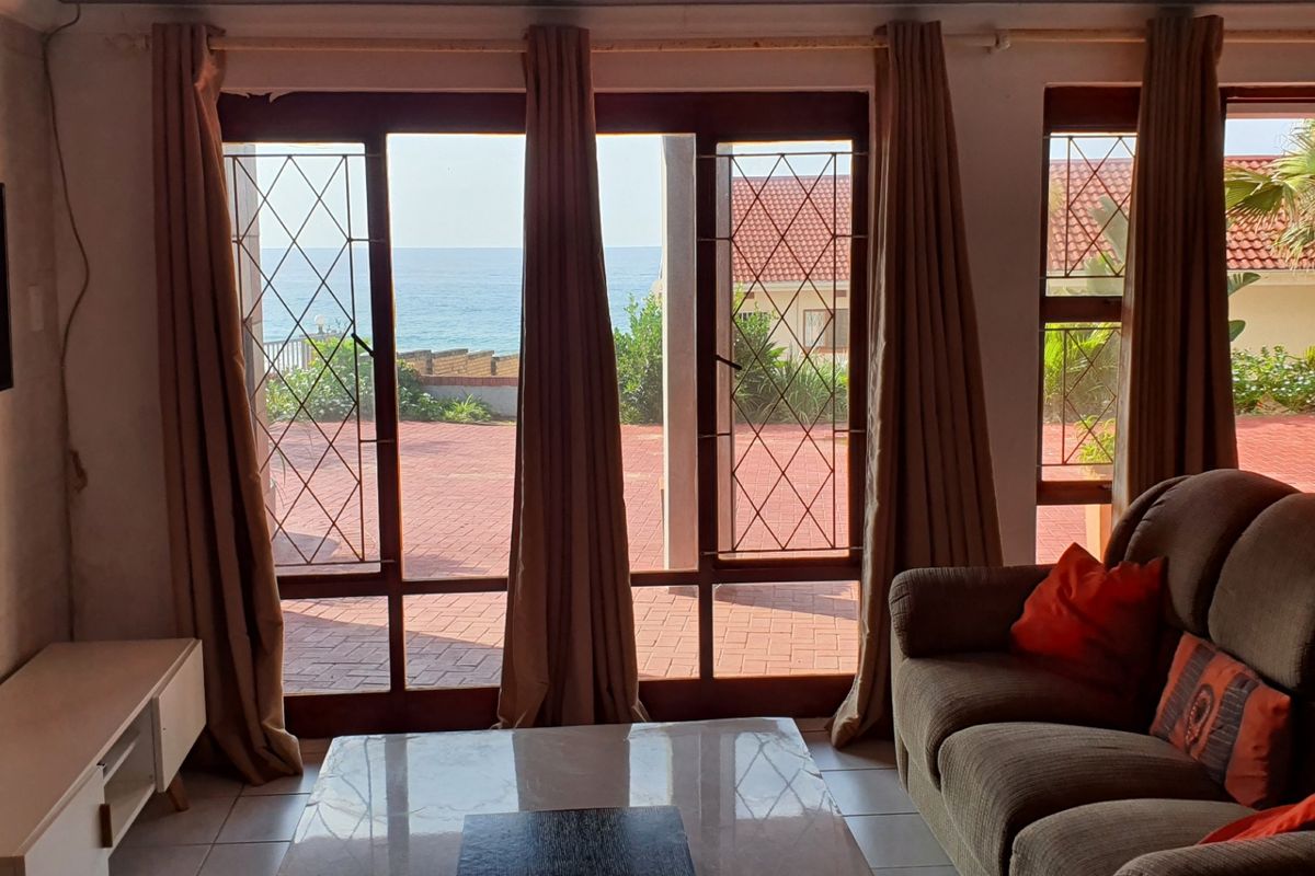 Living room featuring large glass sliding doors with security bars, offering direct access to an outdoor patio and ocean views.