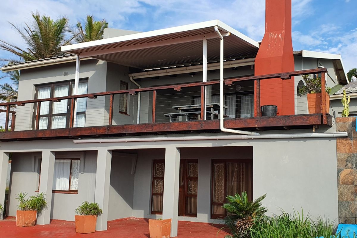Rear elevation featuring a raised wooden deck with a covered patio area, external chimney, and stone-clad feature wall.
