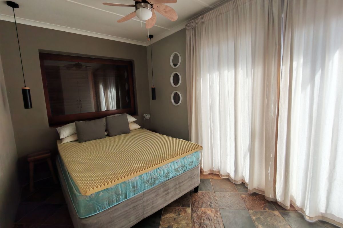 A bedroom featuring slate tile flooring, a ceiling fan, and a built-in headboard with integrated pendant lighting.