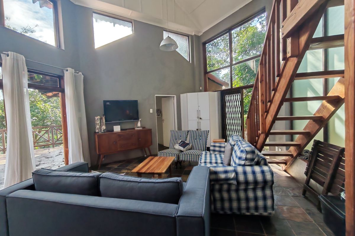Spacious living room featuring a vaulted ceiling, slate tile flooring, a timber staircase, and large windows providing abundant natural light and garden views.