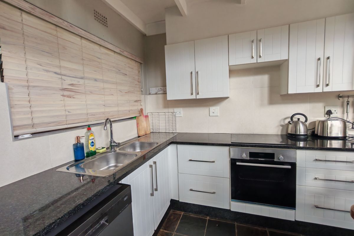 A well-maintained kitchen featuring white cabinetry, granite countertops, a stainless steel double sink, and built-in oven with electric hob.