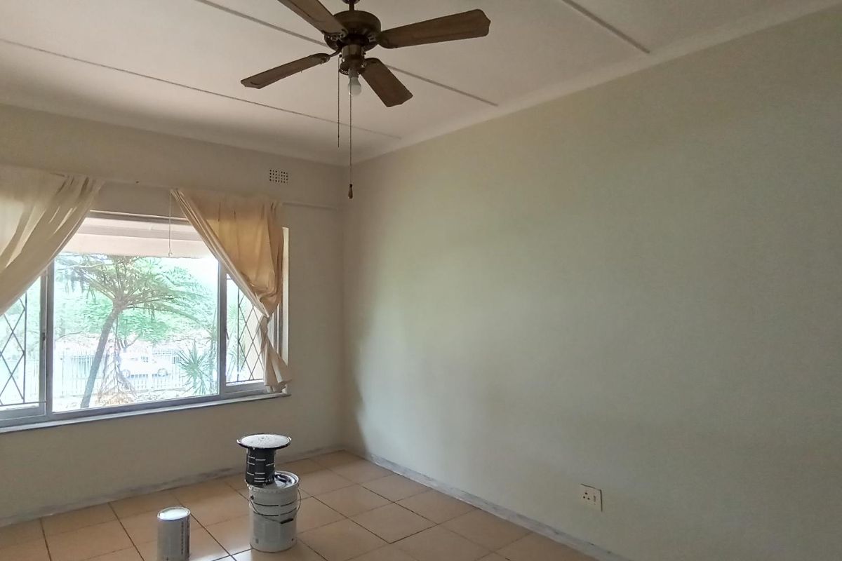A vacant bedroom featuring tiled flooring, a ceiling fan, and a window fitted with security bars.