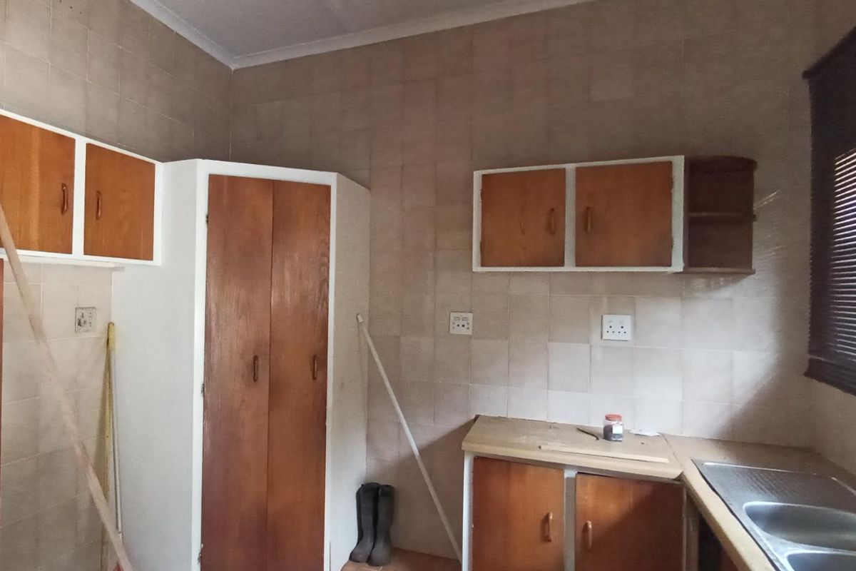A dated kitchen featuring original wooden cabinetry, tiled walls, and a double bowl stainless steel sink, offering significant potential for a modern renovation.