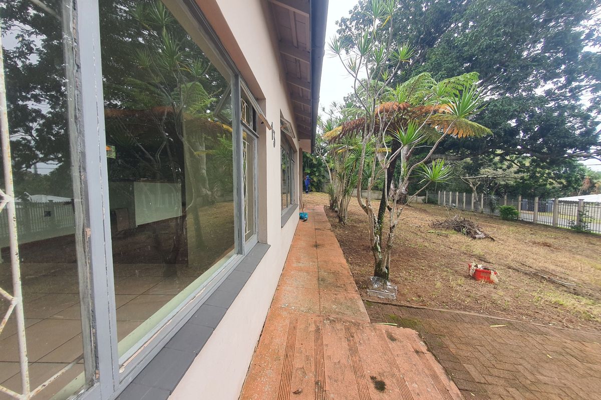 A side view of the property featuring a terracotta tiled pathway, metal-framed windows with security bars, and a spacious rear garden area.