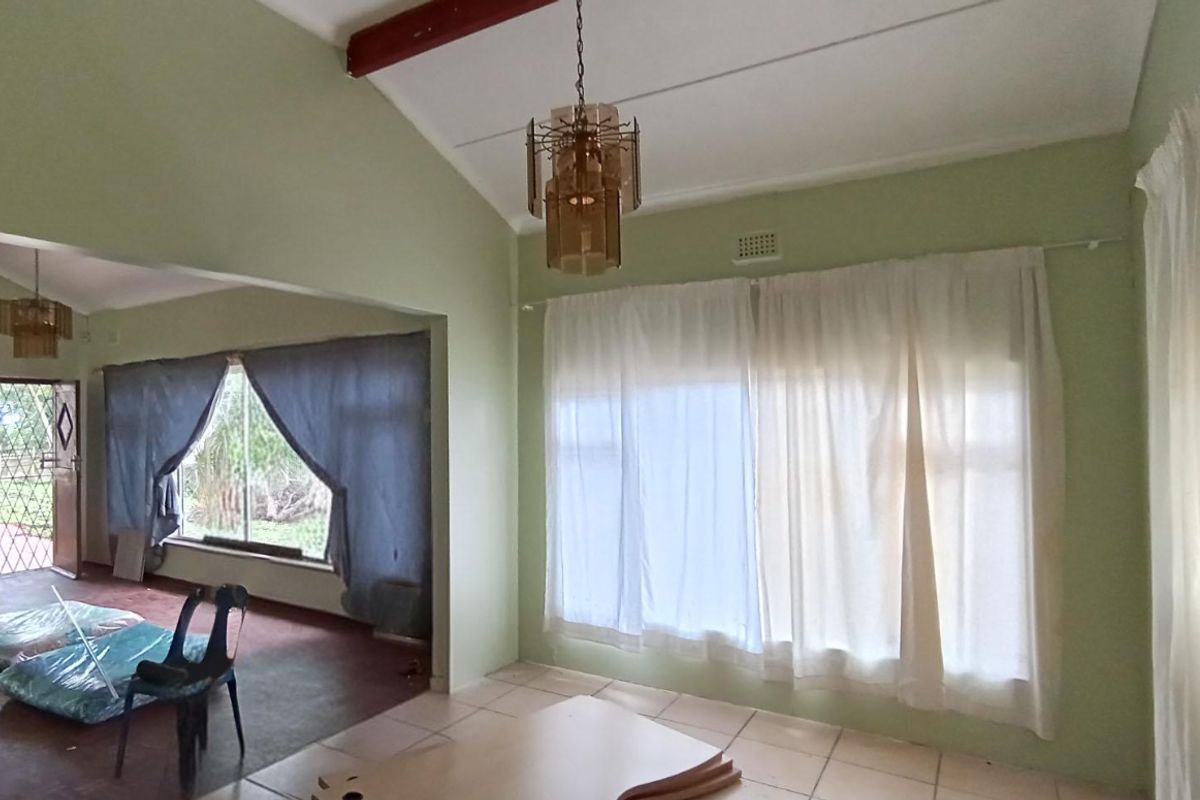 Spacious living area featuring vaulted ceilings with exposed beams, tiled flooring, and an open-plan layout connecting to an adjacent room with security access.