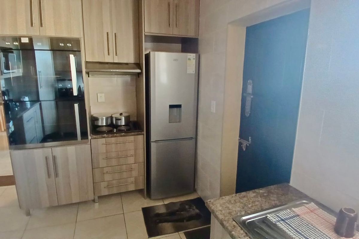 A functional kitchen featuring light wood-toned cabinetry, integrated oven, hob, extractor fan, and tiled finishes with a practical layout.
