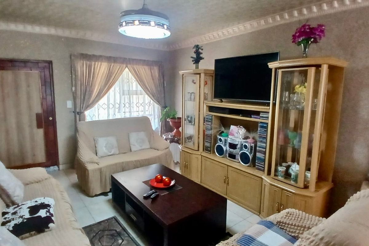 A living room featuring tiled flooring, decorative ceiling cornices, and a security gate over the window.