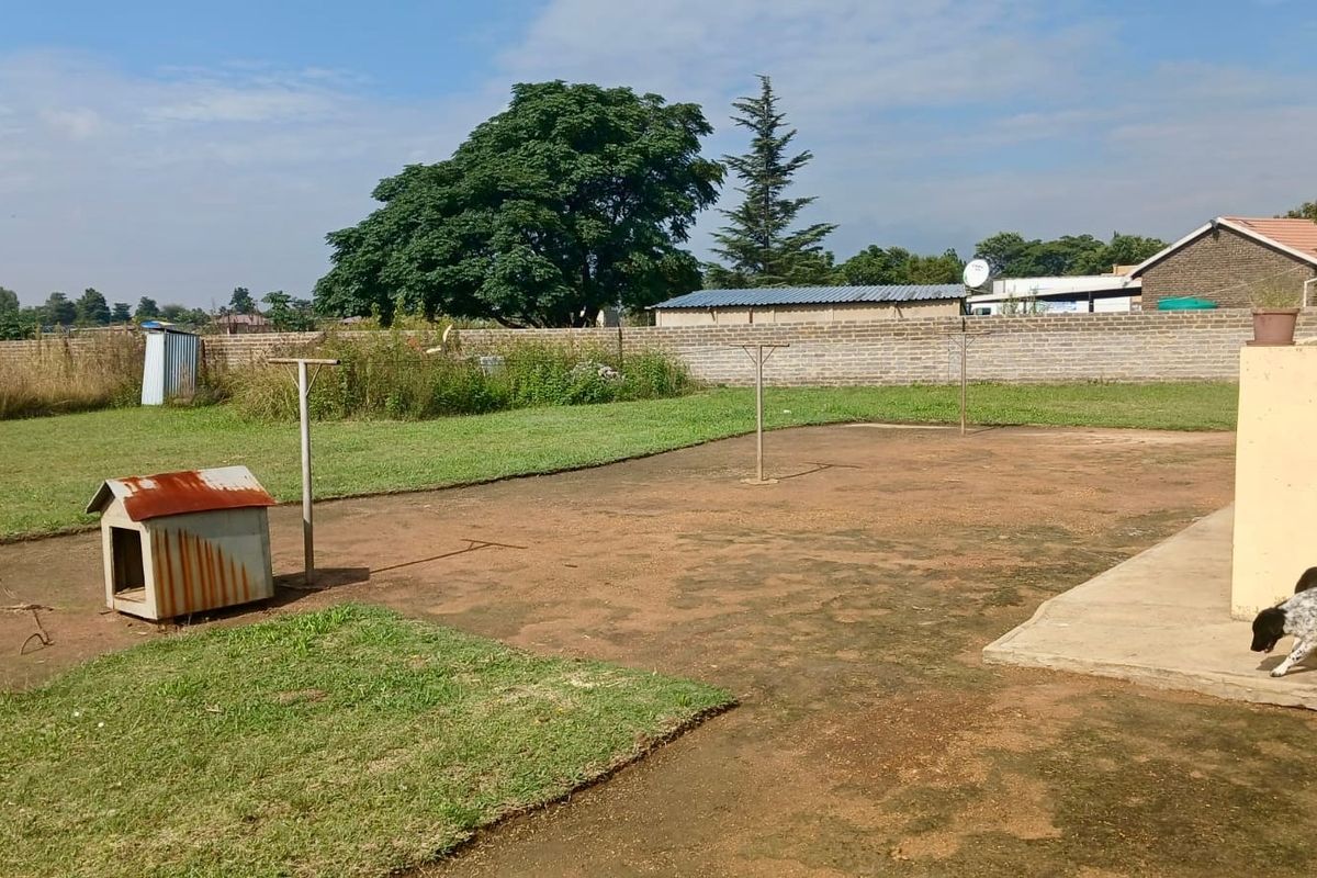 A spacious rear garden area featuring a concrete patio, brick boundary wall, and metal washing line poles, offering potential for landscaping and outdoor improvement.