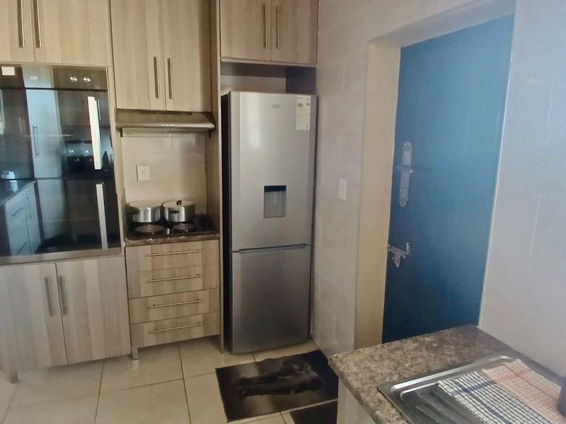 A functional kitchen featuring light wood-toned cabinetry, integrated oven, hob, extractor fan, and tiled finishes with a practical layout.