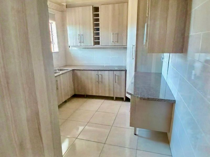 A functional kitchen featuring light wood-tone cabinetry, stone countertops, a double sink, and neutral tiled flooring with a clean tiled splashback.