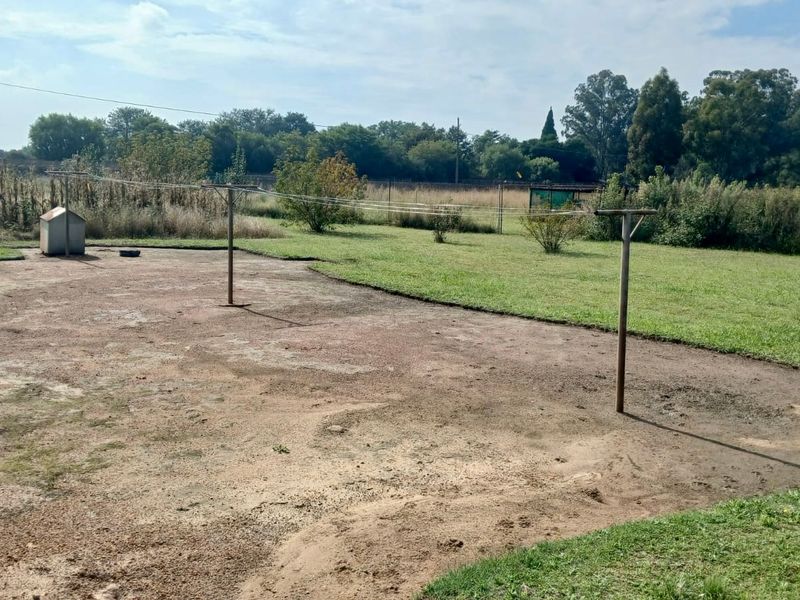 A large, open garden area featuring a fixed washing line and a mix of lawn and bare, eroded ground.