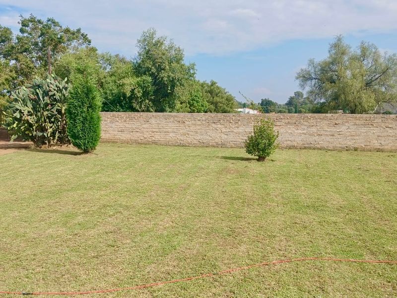 A spacious, level garden area featuring a well-maintained lawn, established greenery, and a secure brick boundary wall with a metal gate.