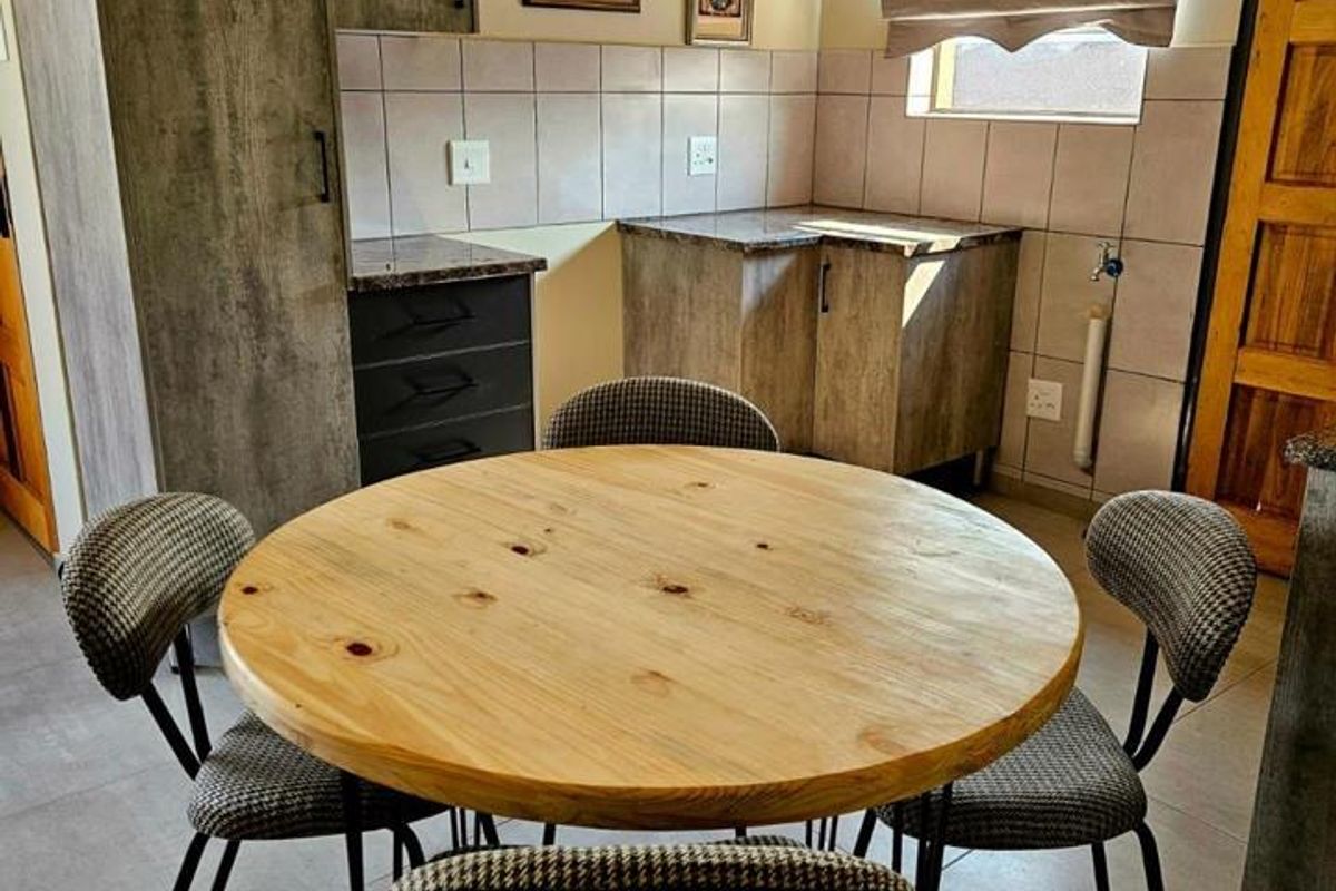 A compact kitchen area featuring modern grey-toned cabinetry, tiled backsplash, and durable floor tiles, currently set up with a small dining table.