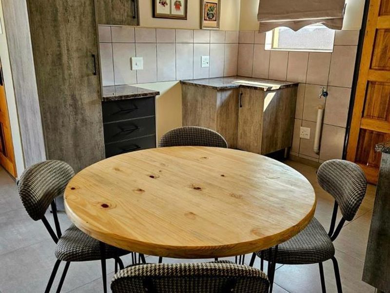 A compact kitchen area featuring modern grey-toned cabinetry, tiled backsplash, and durable floor tiles, currently set up with a small dining table.